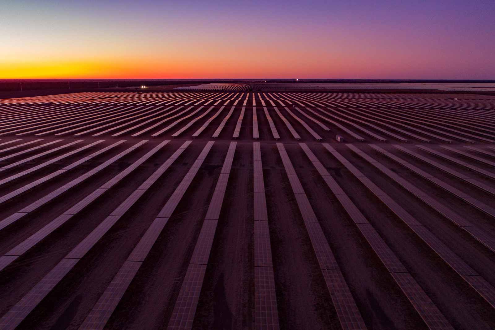 A vast solar panel field at sunset, featuring rows of panels aligning with a colourful sky.