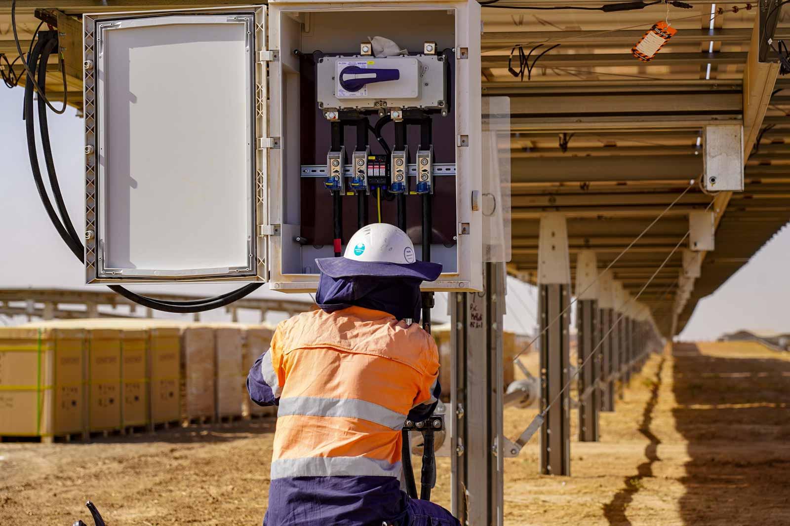 A technician in safety gear inspects electrical connections inside a cabinet at a solar panel installation site.