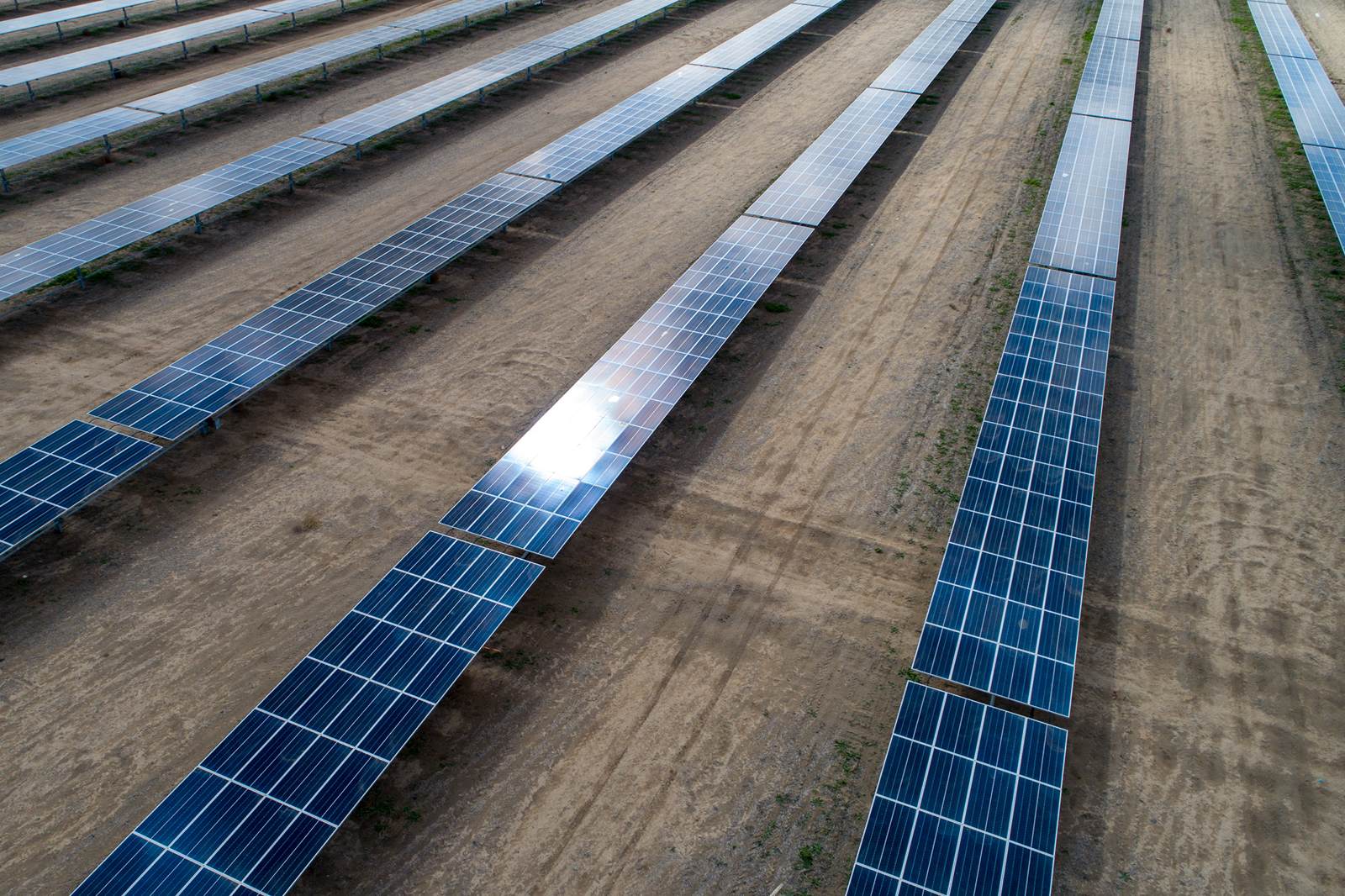 Aerial view of a solar farm with rows of solar panels on a dry landscape.