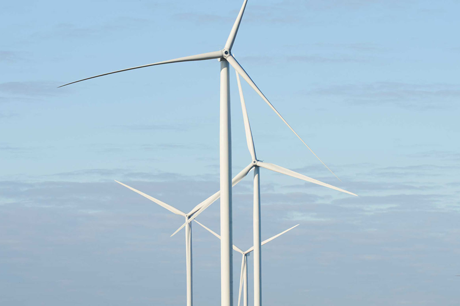 A clear sky with several tall white wind turbines against a light blue backdrop.