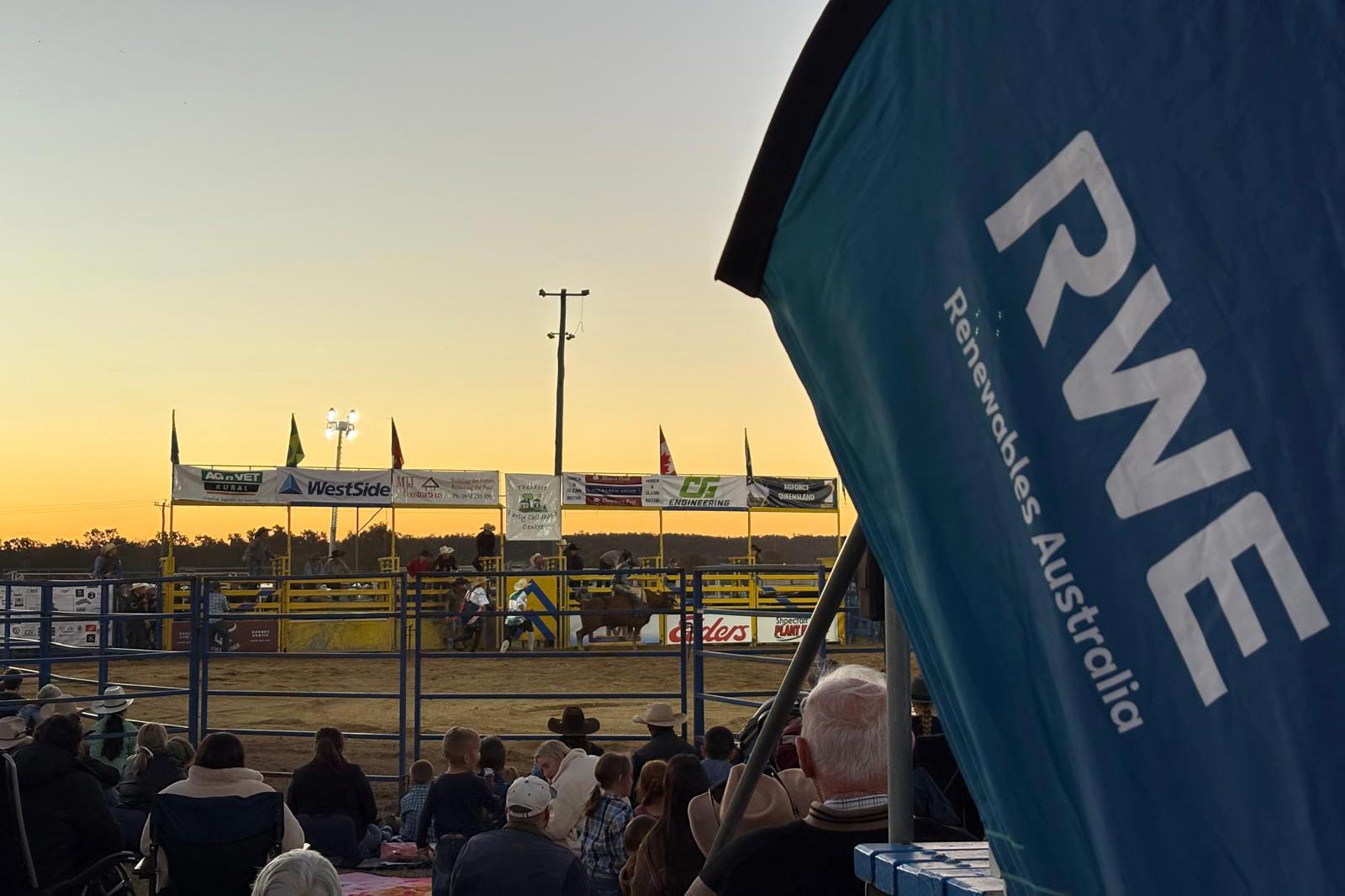 A rodeo event at sunset, featuring bustling spectators and colourful banners, with a prominent RWE banner in the foreground.