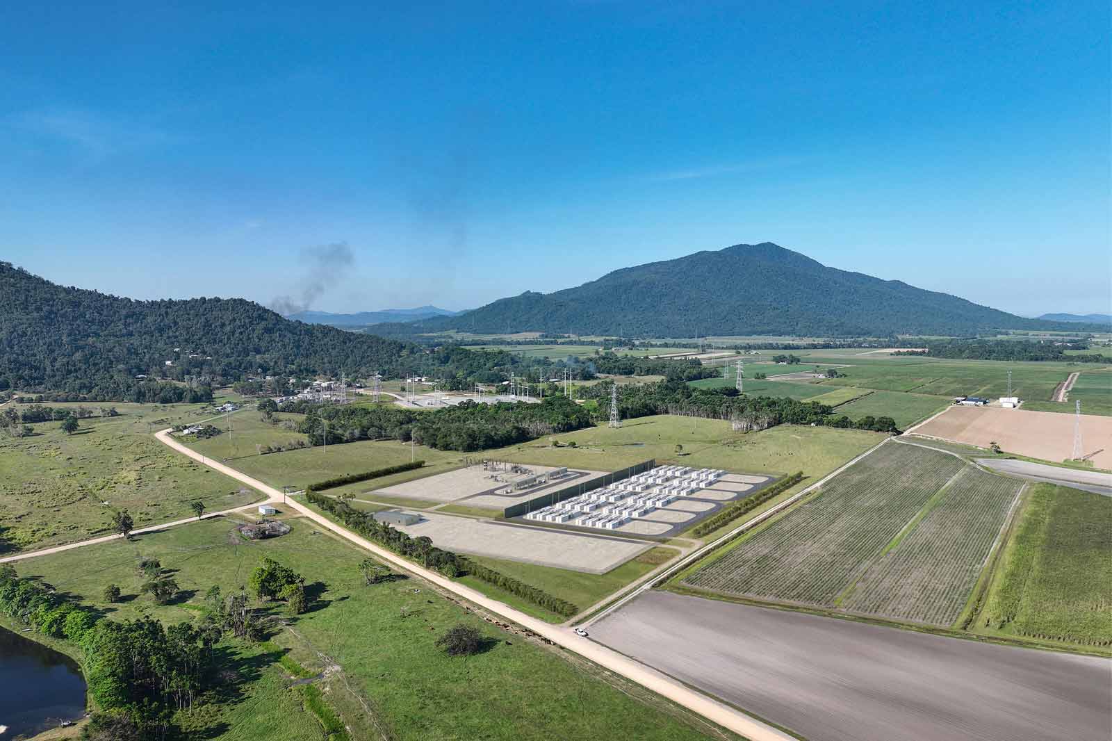 Aerial view of a rural industrial area with gas storage tanks, fields, and mountains in the background.