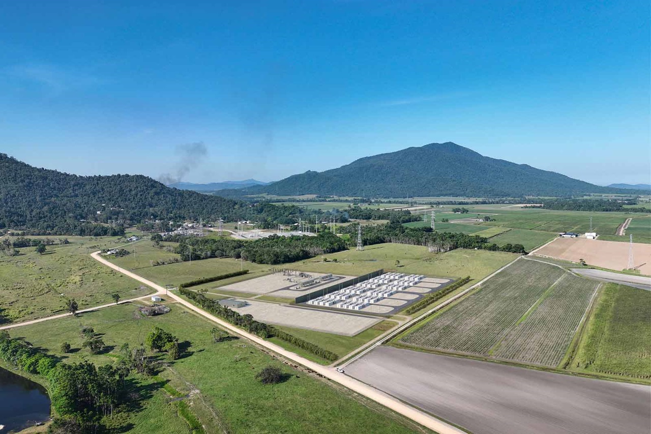 Aerial view of a rural industrial area with gas storage tanks, fields, and mountains in the background.