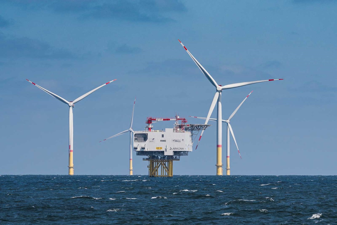 An offshore wind farm with three turbines beside a central platform against a blue sky and calm sea.