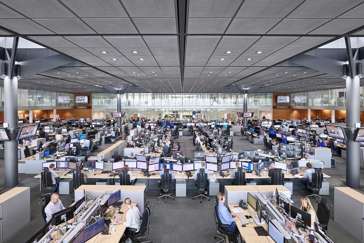 A modern office space filled with numerous workstations and computer monitors being used by staff.